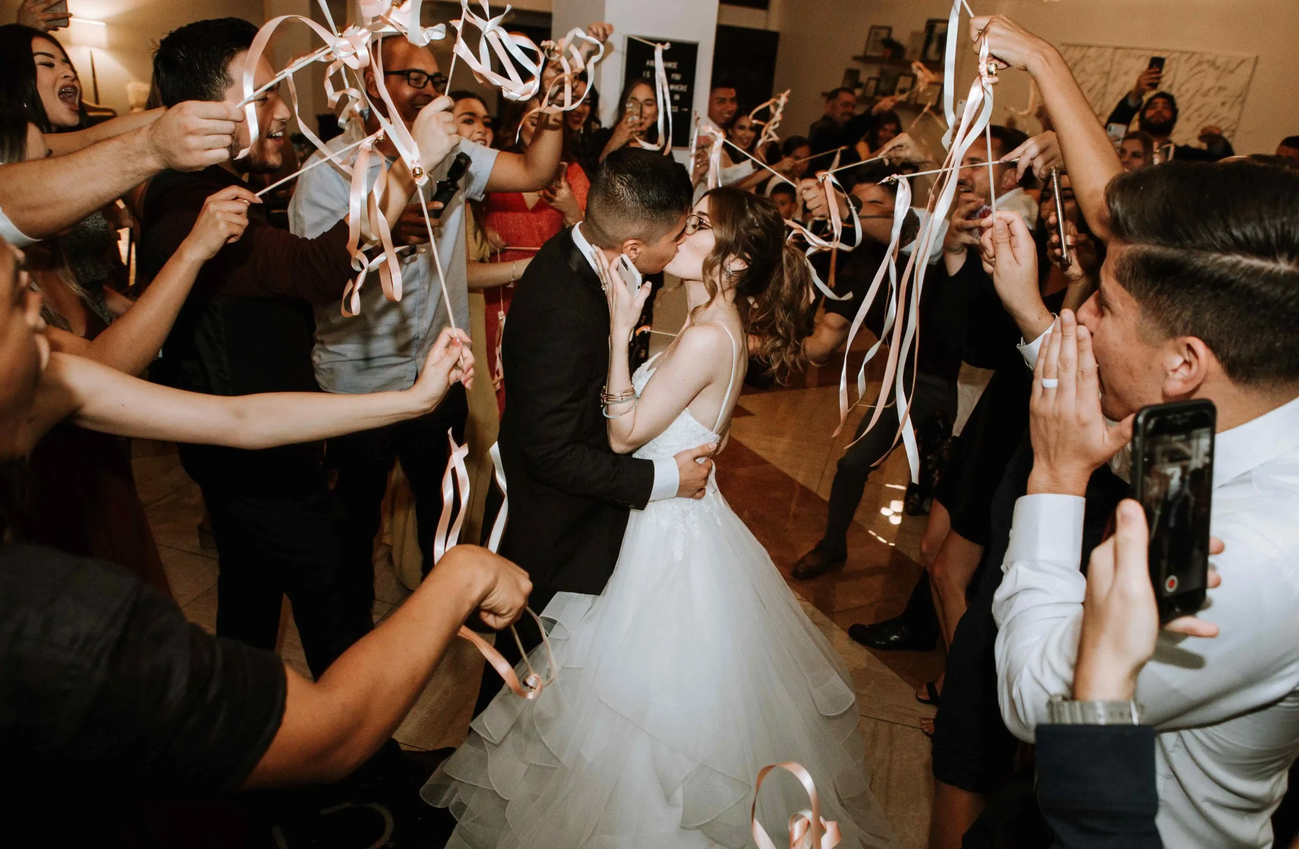 Bride and groom kissing surrounded by friends waving ribbon wands