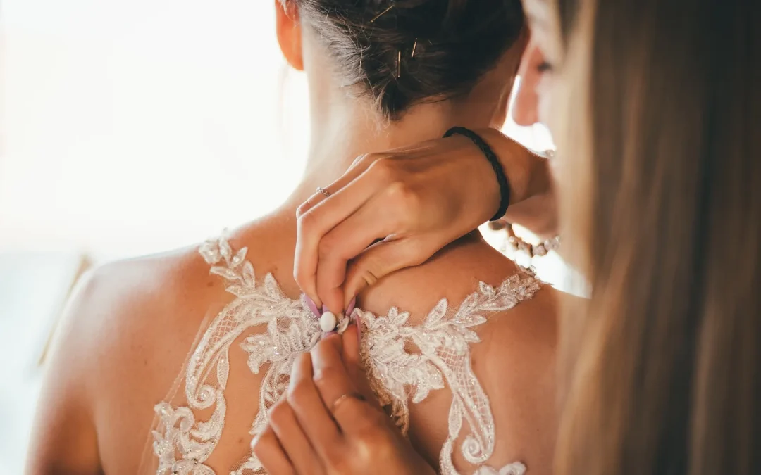 Bridesmaid fastening back of wedding dress